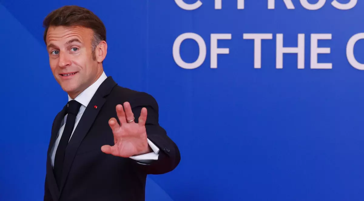 Emmanuel Macron îmbrăcat în costum, în Cipru, în timp ce se retrage de la conferința de presă și le face cu mâna jurnaliștilor