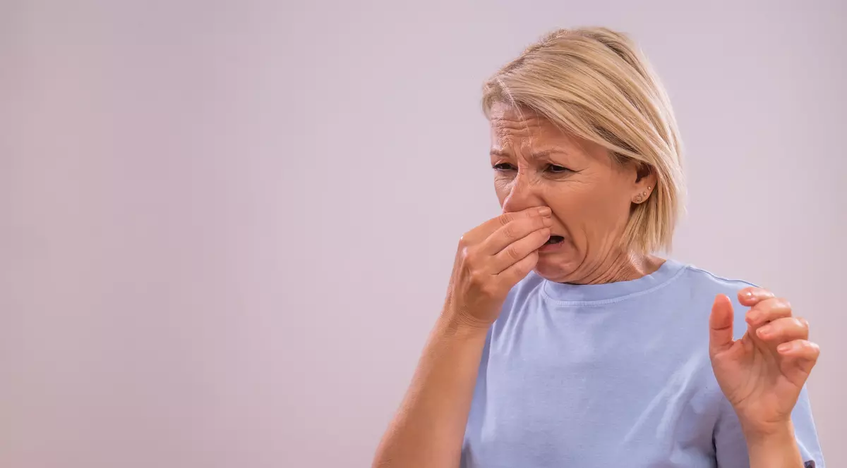 O femeie îmbrăcată într-un tricou albastru se ține de nas din cauza mirosului urât.