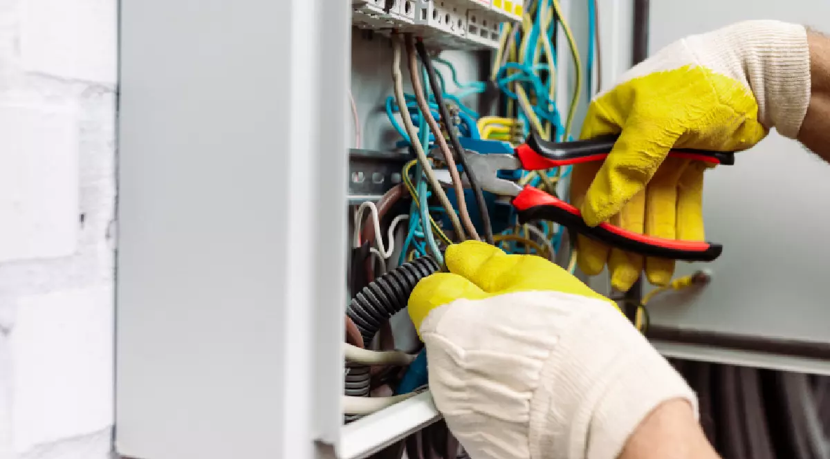 Muncitor cu mănuși ține un clește în timp ce repară o cutie de distribuție electrică