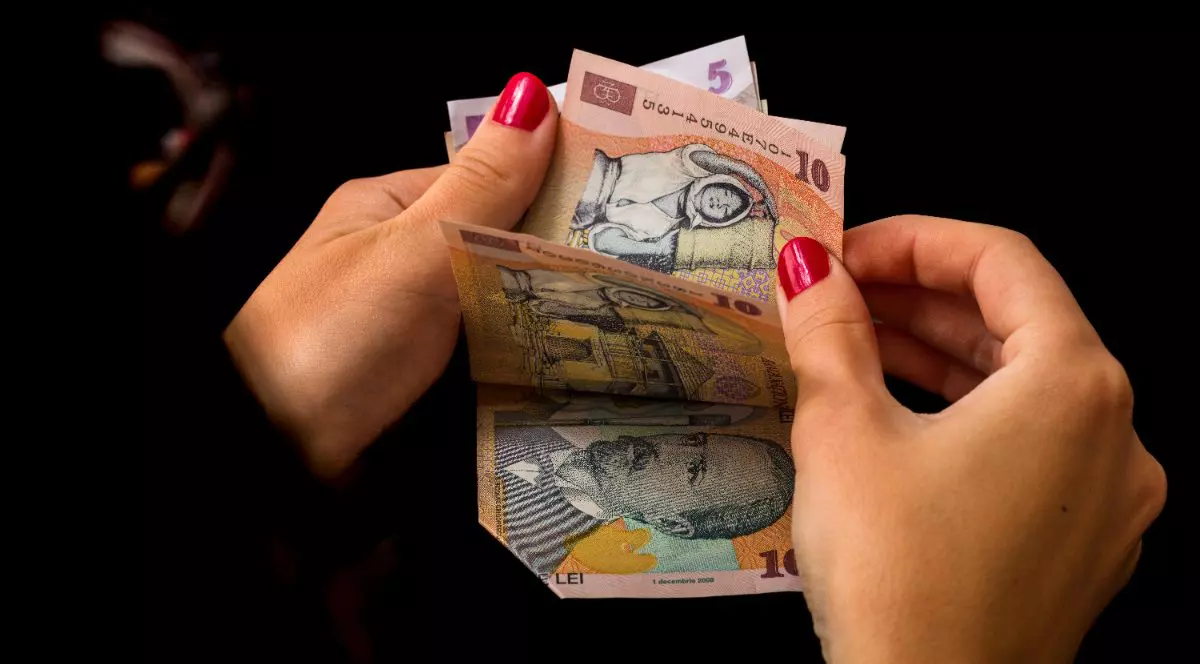 O femeie care ține în mână și numără mai multe hârtii de 10 și 5 lei