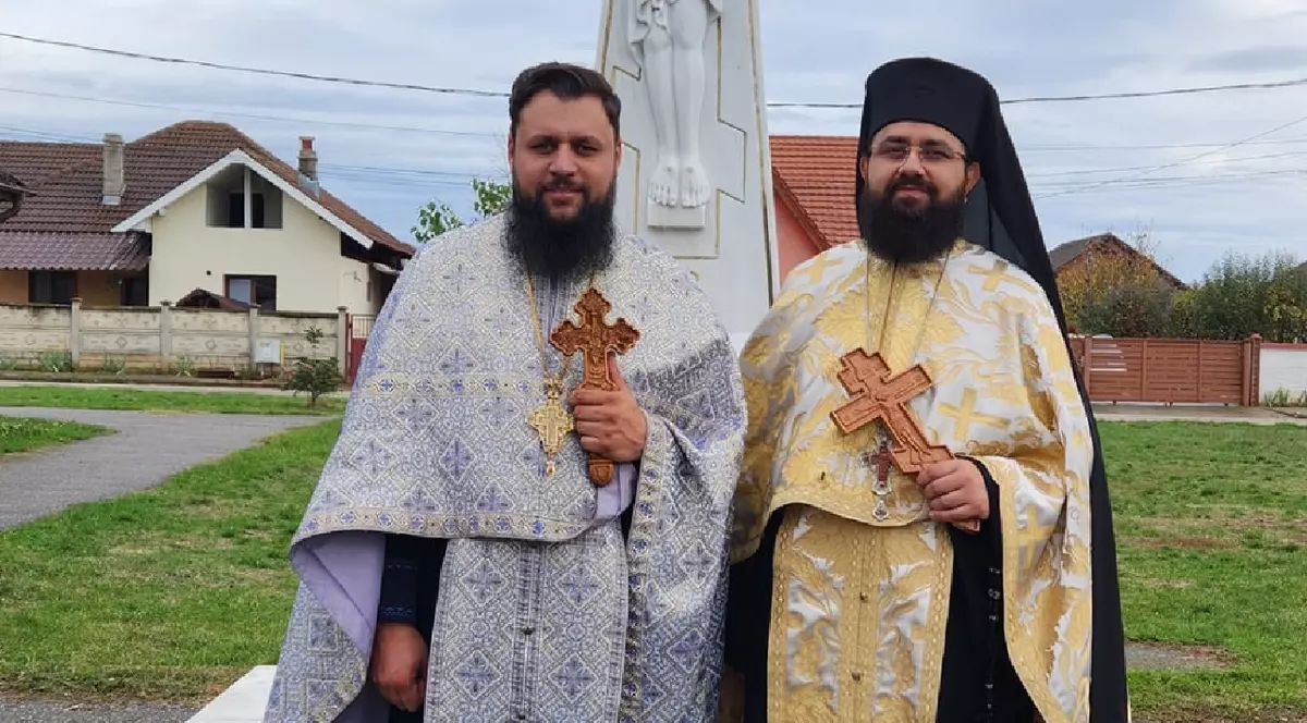 Doi bărbați îmbrăcați în haine de preoți, fiecare dintre ei ține câte o cruce de lemn în mână