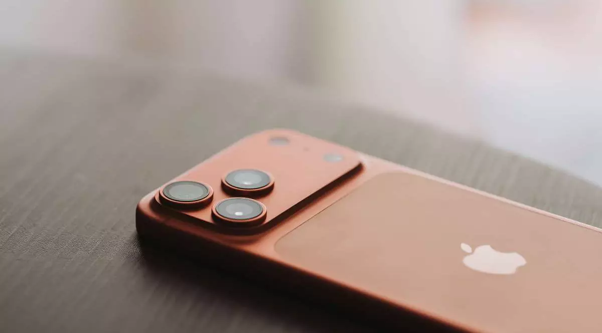 Un iPhone 17 Pro de culoare portocalie, văzut cu partea din spate, aștezat pe ecran pe o masă de lemn.