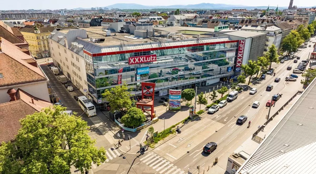 Imaginea prezintă o vedere aeriană a unui magazin de mobilier XXXLutz din Viena, situat la o intersecție circulată.