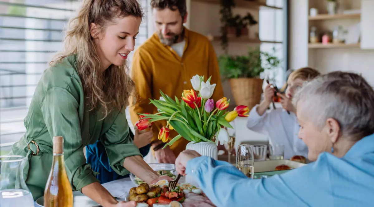 O familie așezată la masa de Paște, în timp ce servesc aperitivul, pe masă au o vază cu lalele