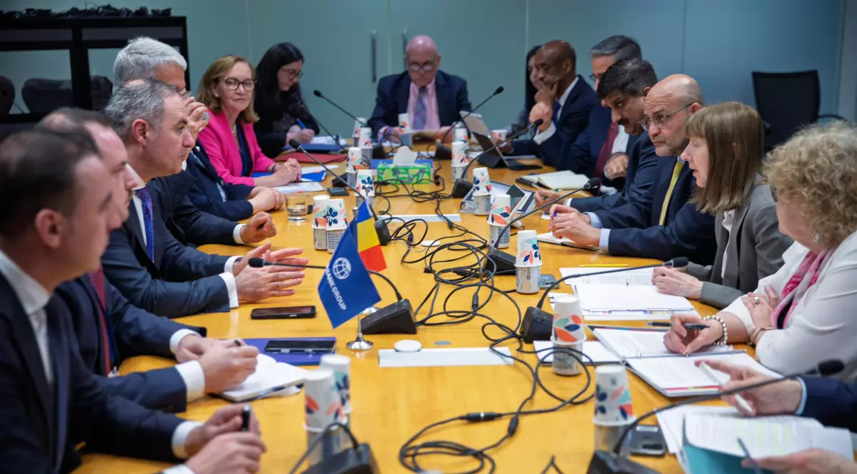 Mai mulți oficiali stau la o masă de negocieri, discutând în cadrul unei întâlniri formale între delegații. Pe masă se află documente, microfoane și steaguri, sugerând o discuție oficială pe teme economice sau politice.