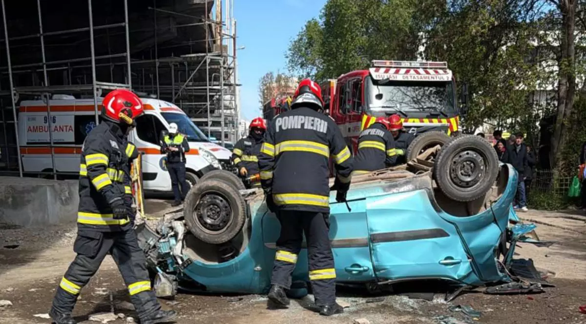 Mașina de culoare albastră, prăbușită la baza podului Bucium din Iași, pe plafon, cu pompieri în uniforme care lucrează să scoată victimele din mașină