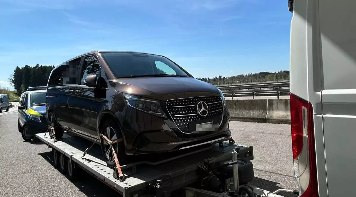 Un Mercedes V-Class negru, urcat pe o remorcă, oprit de vameși pe o autostradă, în spate se vede o masina de politie, cerul este albastru