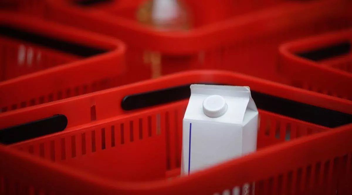 O cutie albă de lapte se vede în mijlocul unui coș roșu de cumpărături, iar în jur sunt alte coșuri roșii