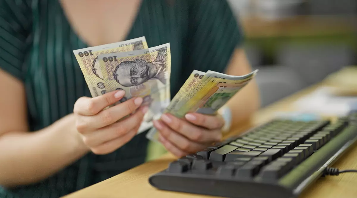 O femeie cu rochie verde care stă la birou și numără mai multe hârtii de 100 de lai