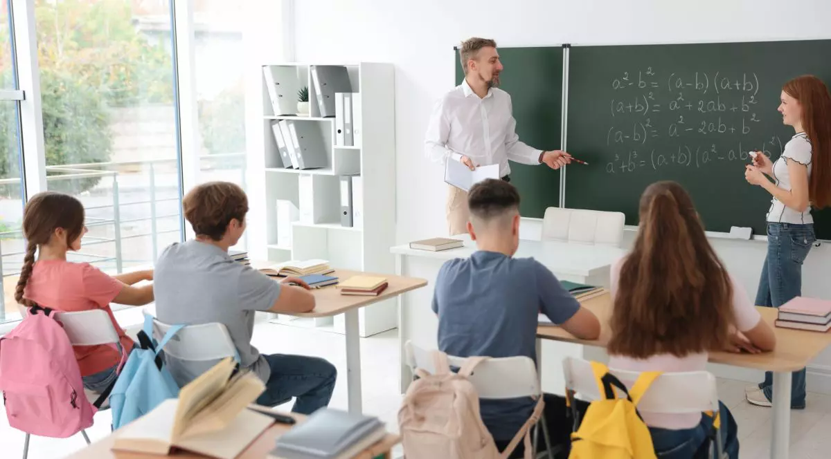 Profesor de matematica in clasa la tabla alaturi de un elev