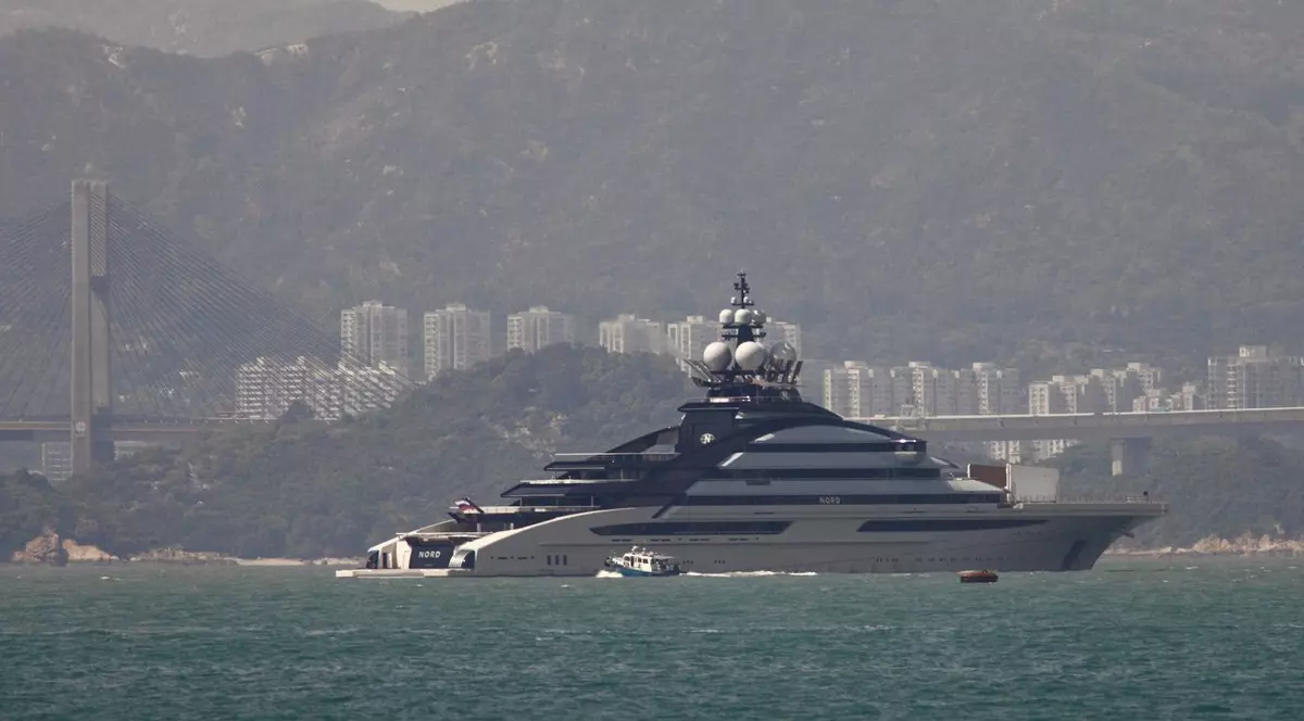 O imagine panoramică surprinde superiahtul de lux Nord navigând pe apele din largul coastelor Hong Kong-ului, având pe fundal un peisaj urban dens, un pod suspendat impunător și munți estompați de ceață.