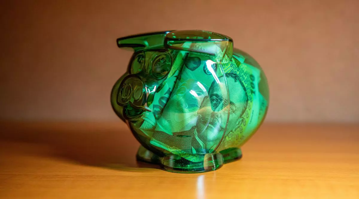 Pușculiță din sticlă de culoare verde transparent cu bancnote de 100 de lei în interior, pe o masă de culoare maro