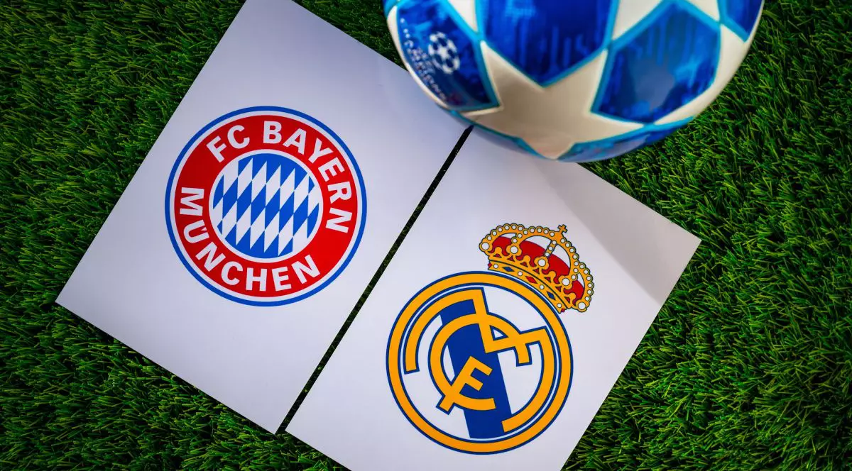 Imagine creativă cu logo-urile Real Madrid și Bayern Munchen pe terenul de fotbal și o minge de Champions League lângă