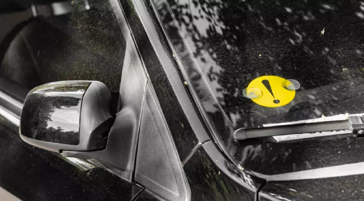 Mașină neagră care are pe geamul din față un semn de șofer începător.