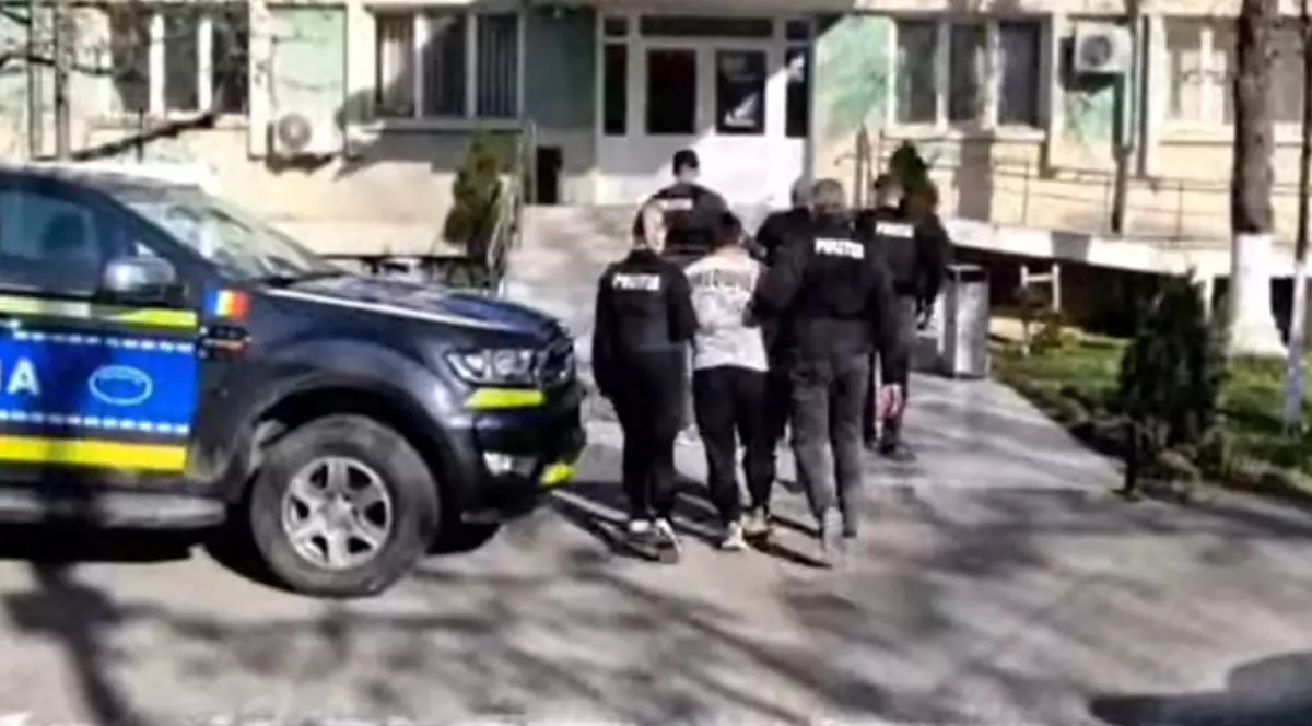 Cei doi suspecți reținuți, escortați de polițiști, în fața sediului Poliției din Slatina, cu o mașină de Poliție în față