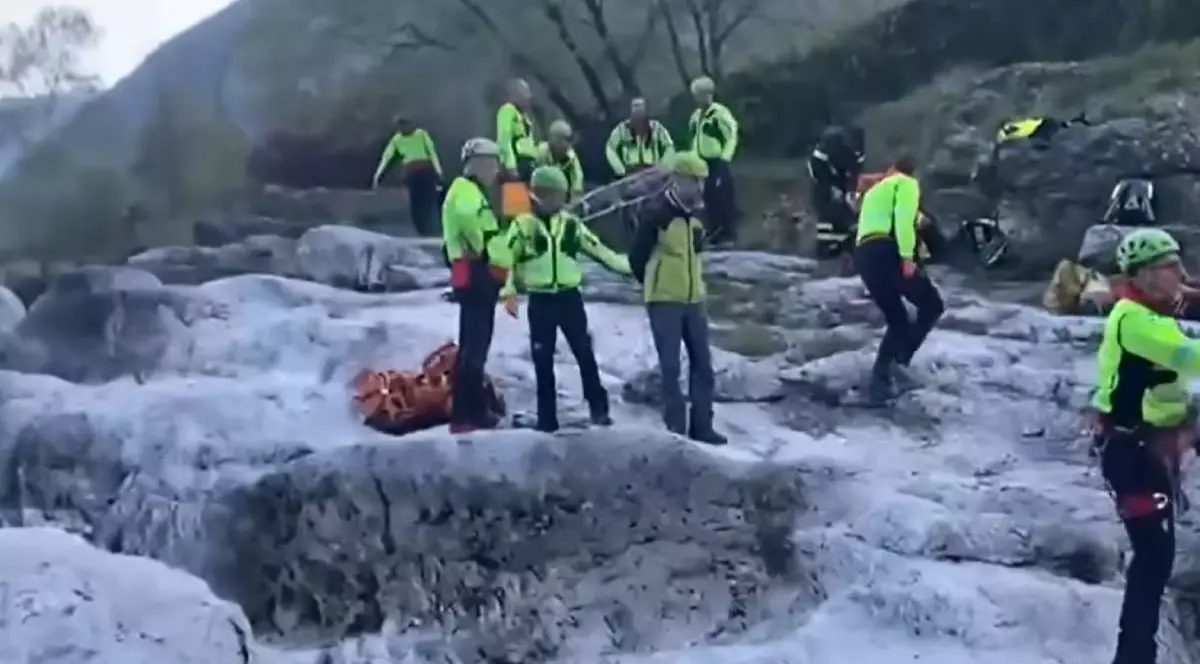 Imagini cu mai multi salvatori, in haine verzi fosforescente, pe pietrele unui rau, in timpul unei misiuni de salvare in Italia