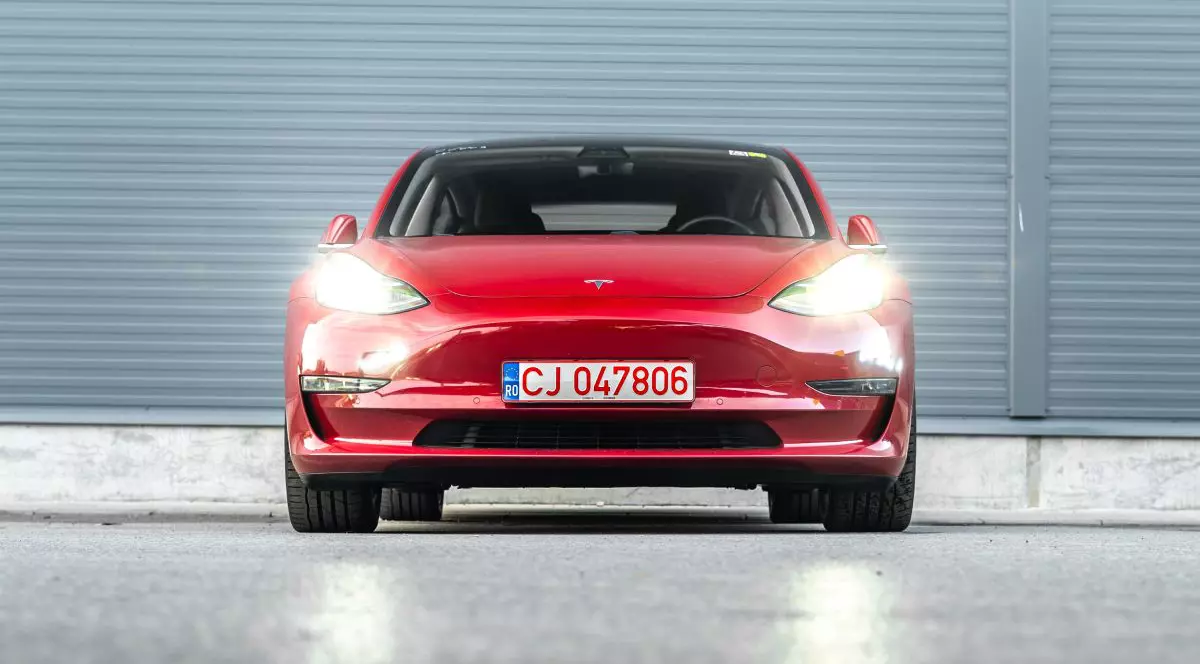 Tesla Model 3, de culoare roși, din față, cu farurile aprinse, cu numere provizorii de Cluj