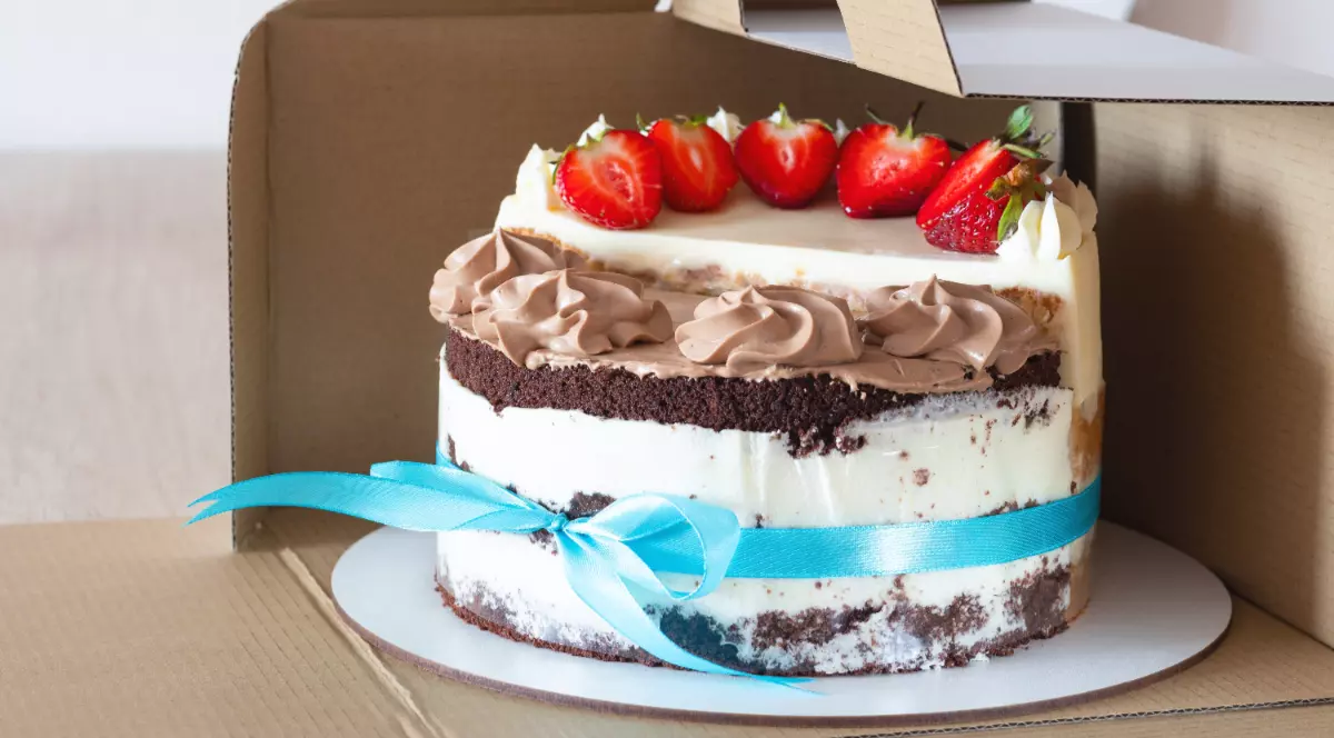 Un tort de vanilie cu ciocolată și frișcă, decorat u căpșuni și pus într-o cutie de carton