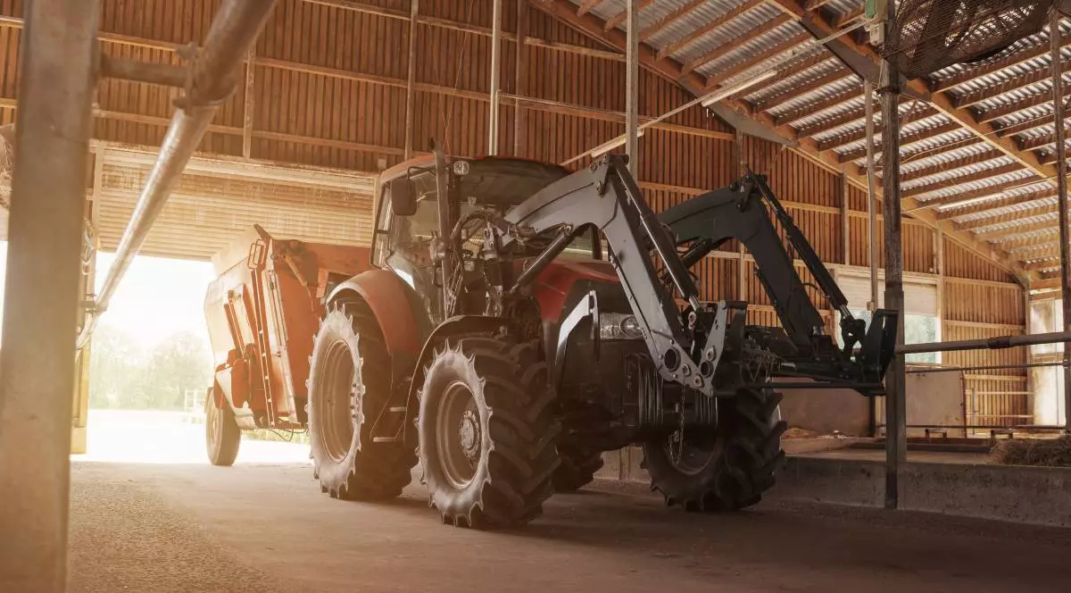 Un tractor modern roșu și negru, echipat cu încărcător, parcat într-un hambar spațios din lemn