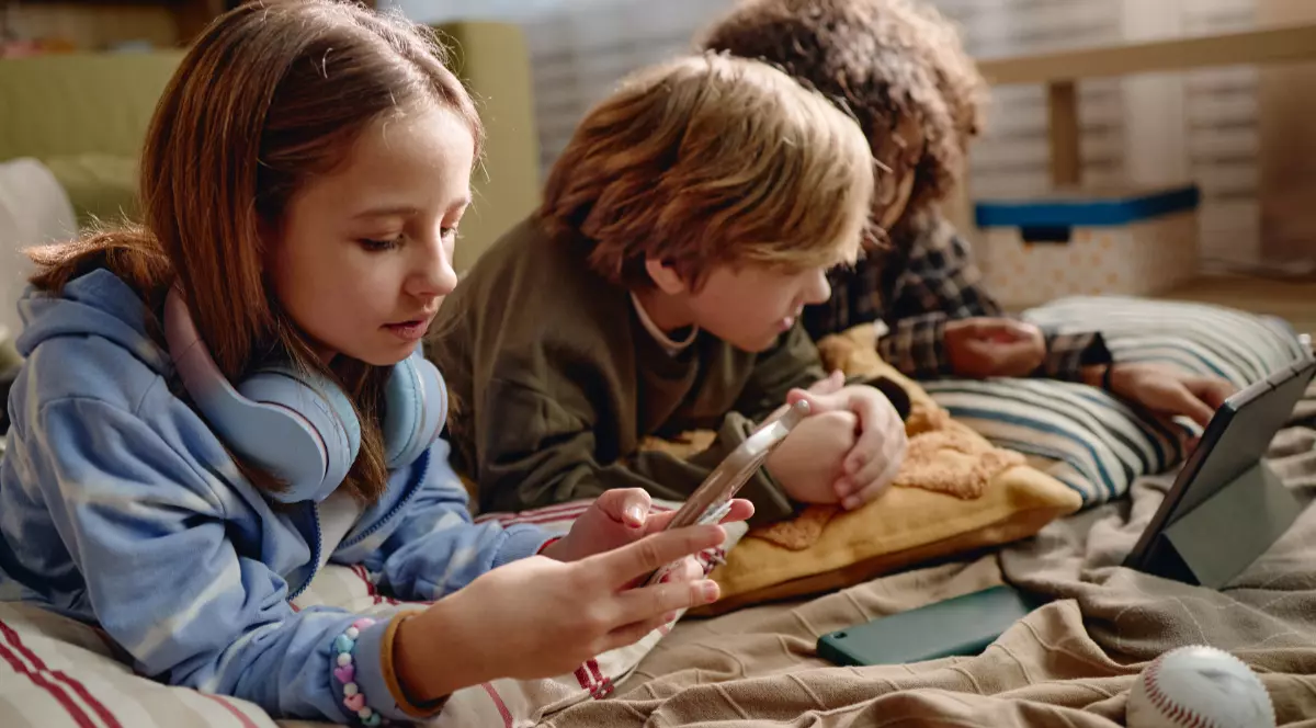 Trei copii, o fată și doi băieți, care stau în pat și se uite pe rețelele sociale pe telefin