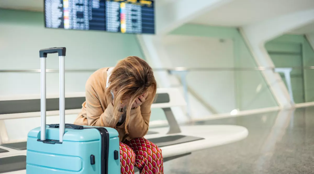 O femeie care stă pe scaun în aeroport, cu valiza lângă ea, supărată după ce a pierdut o vacanță