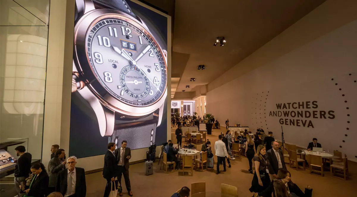 Un afiș cu un ceas mare expus pe lîngă care trec oamenii careu au venit la Watches and Wonders din Geneva.