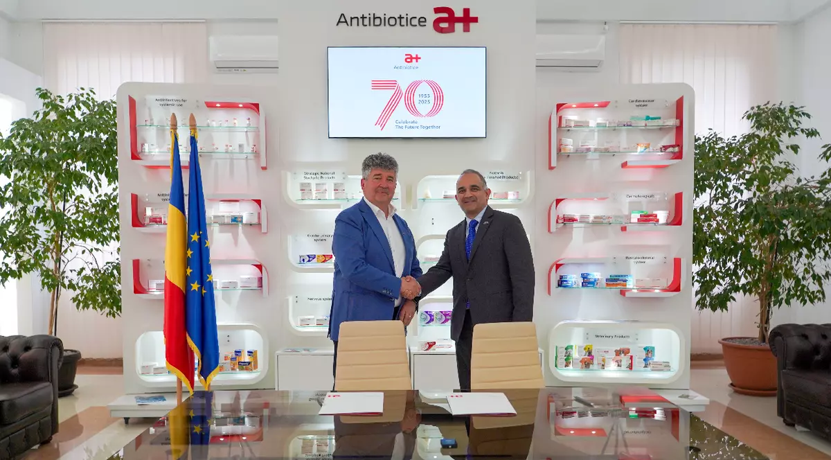 Doi bărbați își strâng mâna într-un birou unde se vede sigla Antibiotice Iași și steagul României și al UE