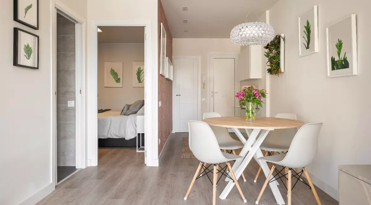 Un apartament mic cu mobila alba, masa si scaunele sunt albe, intrarea in dormitor se face direct din living