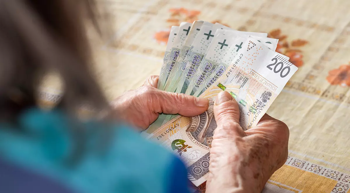 Mâinile unei femei căreia nu i se vede fața și care ține bani polonezi.