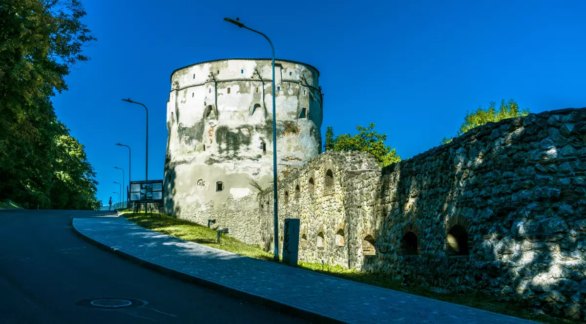 Bastionul Postăvarilor din Brașov, afară este soare, copacii au frunze verzi și cerul este senin.