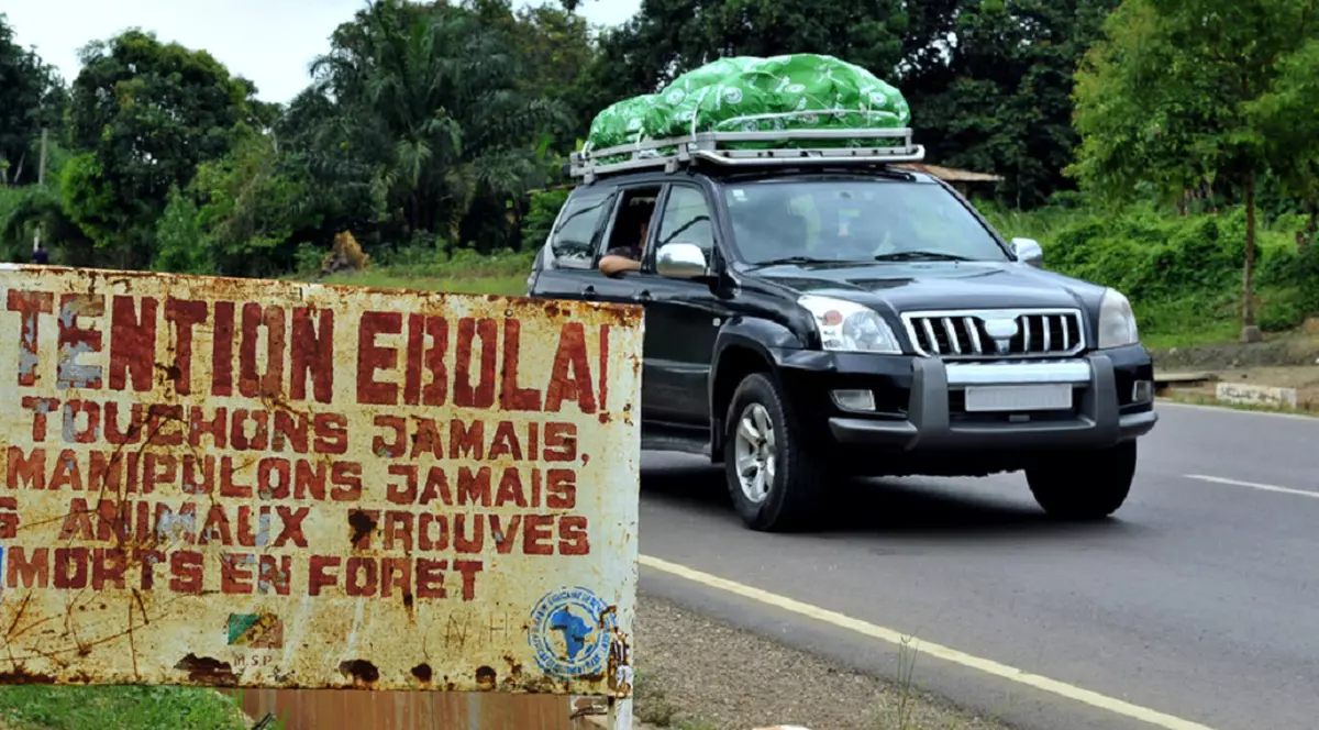 Ce este Ebola, cum se transmite, cât de mortal e virusul și ce tratamente există - Un panou ruginit pe marginea unui drum avertizează în franceză împotriva atingerii animalelor moarte din cauza virusului Ebola, în timp ce o mașină de teren trece pe lângă el