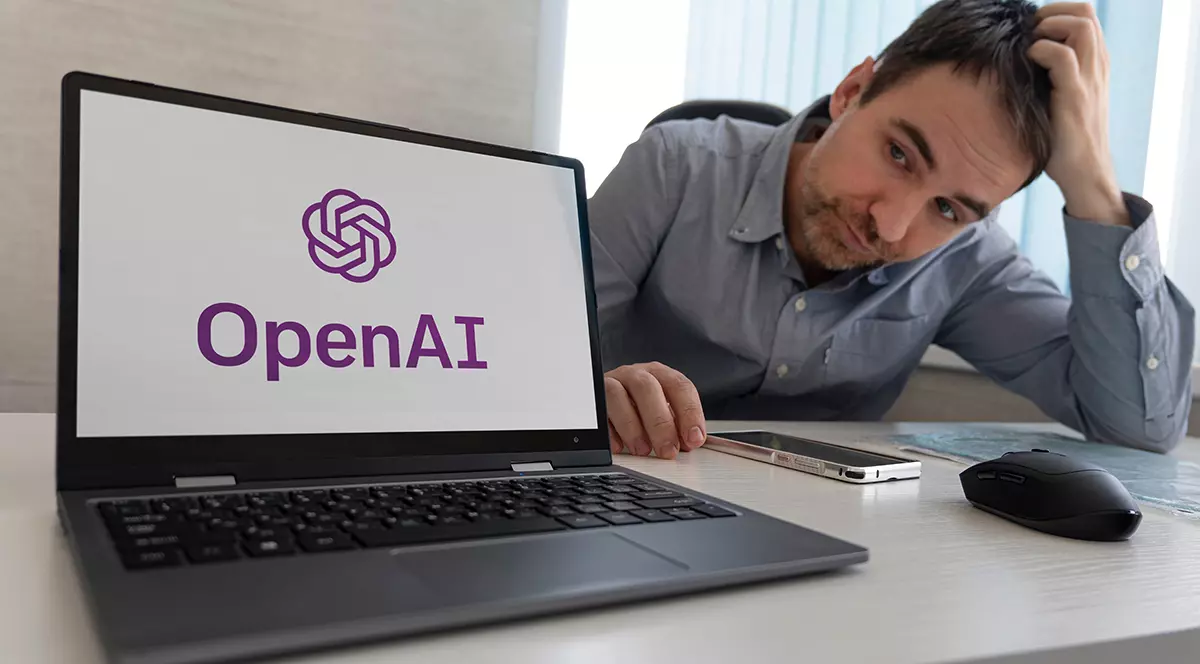 Sigla OpenAI pe ecranul laptopului lângă un angajat trist așezat la locul de muncă