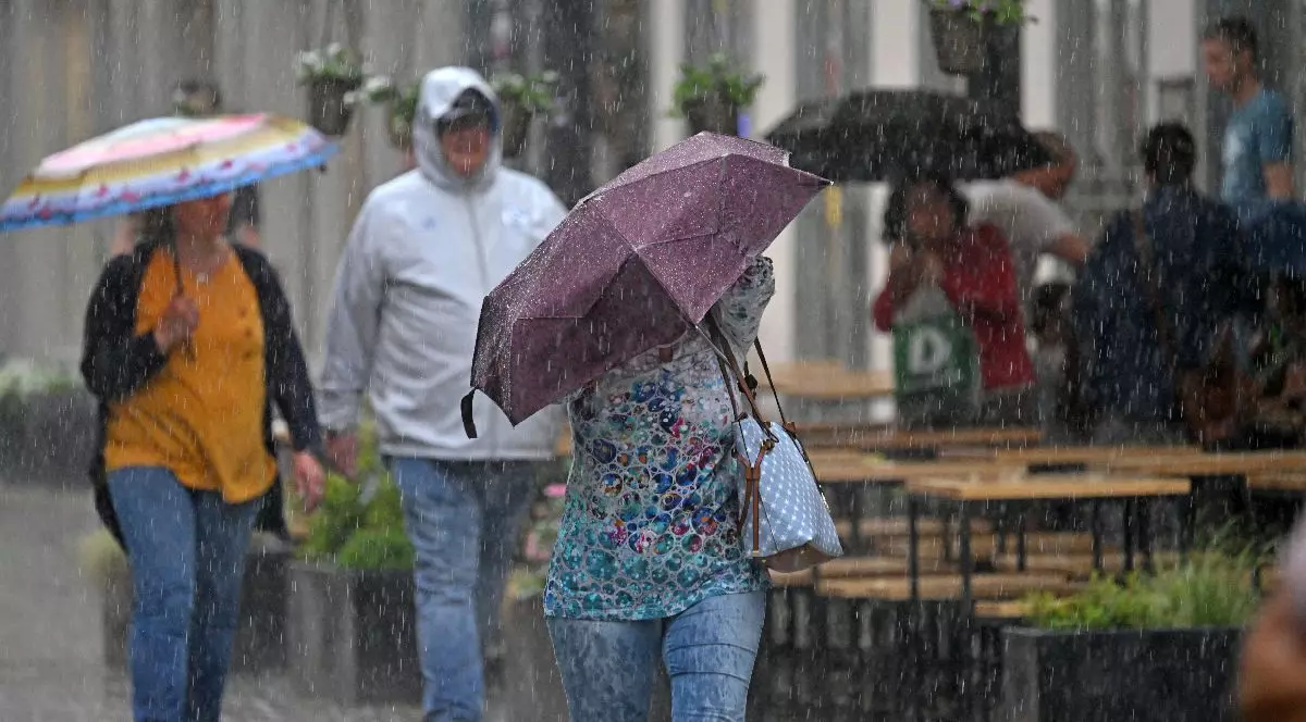 Imaginea arată mai multe persoane pe stradă, care se adăpostesc sub umbrele de ploaia torențială