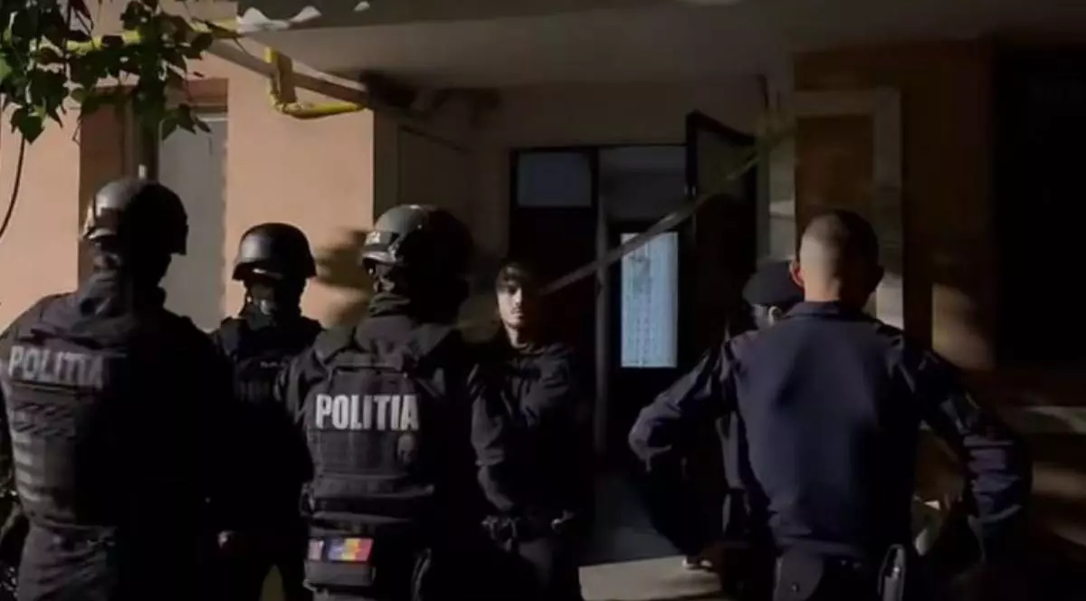 Mai mulți polițiști și luptători ai trupelor speciale stau în fața intrării unui bloc, noaptea, în timpul intervenției din cazul crimei din Târgu Jiu.