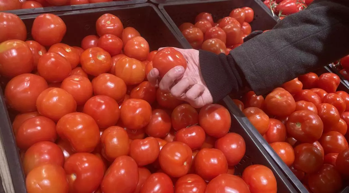 Un client într-un supermarket a luat în mână o roșie, iar în prim-plan se văd mai mult lădițe cu aceste legume