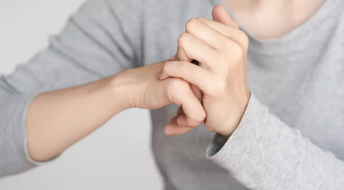 De ce simțim nevoia să „trosnim” degetele - O tânără, îmbrăcată cu o bluză gri, își trosnește degetele
