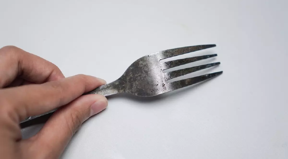 De ce tacâmurile de inox prind puncte de rugină în mașina de spălat vase - O mână ținând o furculiță din metal veche, pătată și ruginită, pe un fundal alb neutru