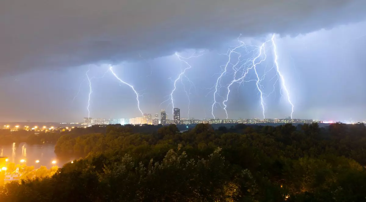 Imagine aeriană cu o furtună cu fulgere peste un oraș, nori negri pe fundal și orașul luminat, pe timp de noapte