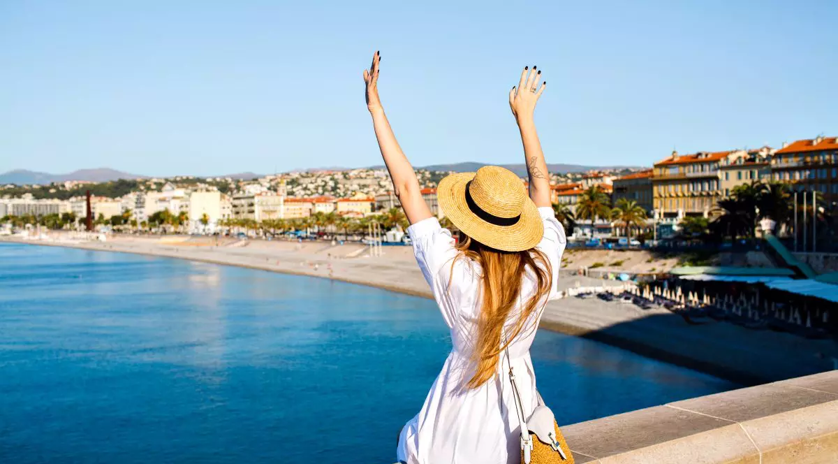 Touristic picture of happy elegant woman posing back, put her hand in the air and enjoying amazing view in France Cannes beach, traveling goals, elegant glamour clothes, summertime.