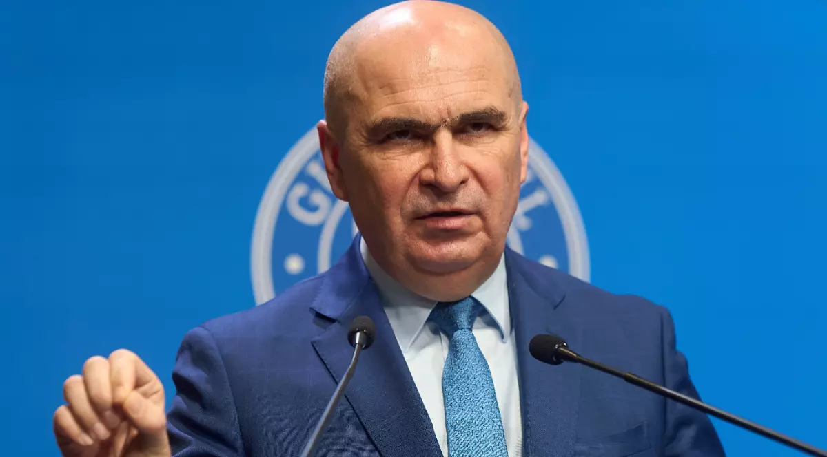 Ilie Boloajn îmbrăcat ân costum albastru, gesticulând în fața unui microfon