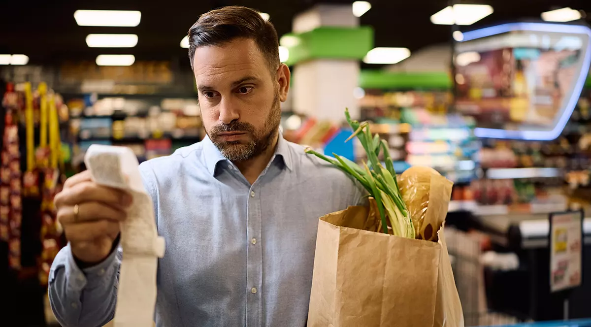 Omul îngrijorat verifică factura după ce cumpără alimente la supermarket