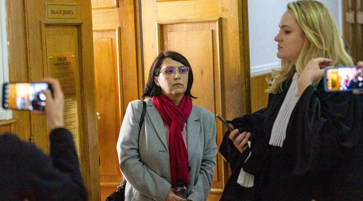 Laura Dronca cu un fular grena la gât și un pardesiu gri iese din sala de judecată fiind însoțită de avocata ei.