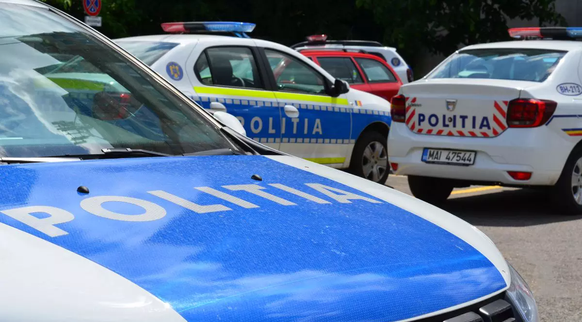 Imagine ilustrativă cu trei mașini ale Poliției Române, în prim plan capota albastră a uneia dintre ele pe care scrie POLITIA