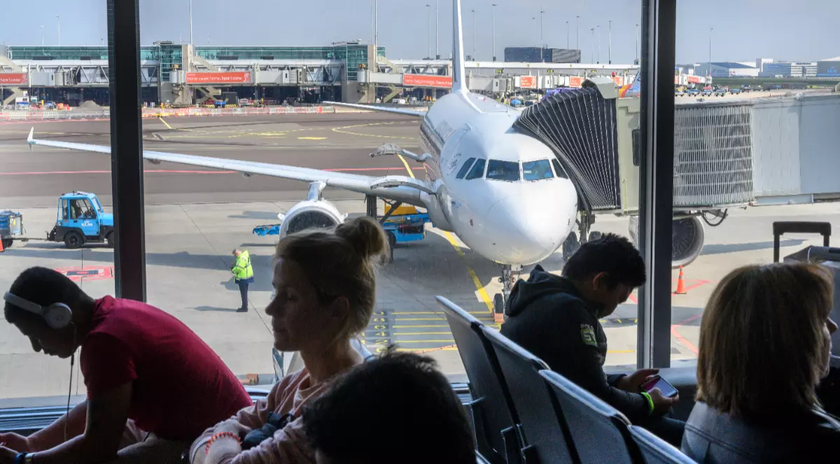 Un Airbus A321 stă pe pistă, în timp ce călătorii așteaptă în zona Plecări a aeroportului
