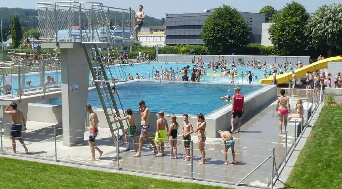 Un grup de copii așteaptă să urce pe trambulină pentru a sări în apă, la piscina din Porrentruy