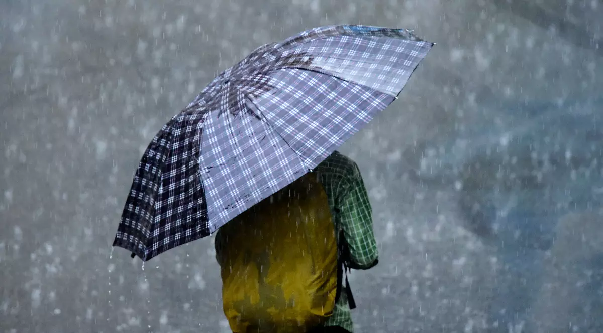 Imaginea arată o persoană care se adăpostește sub o umbrelă, în timpul unei ploi torențiale