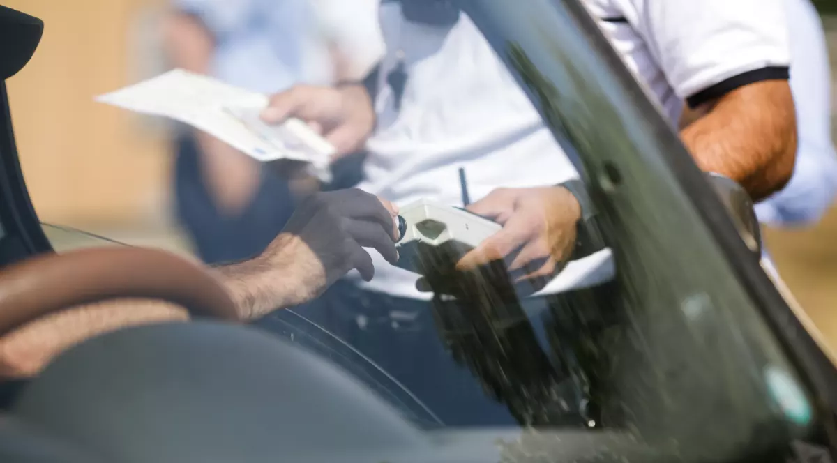 Un polițist care a oprit un șofer în trafic și îi verifică alcoolemia cu aparatul etilotest