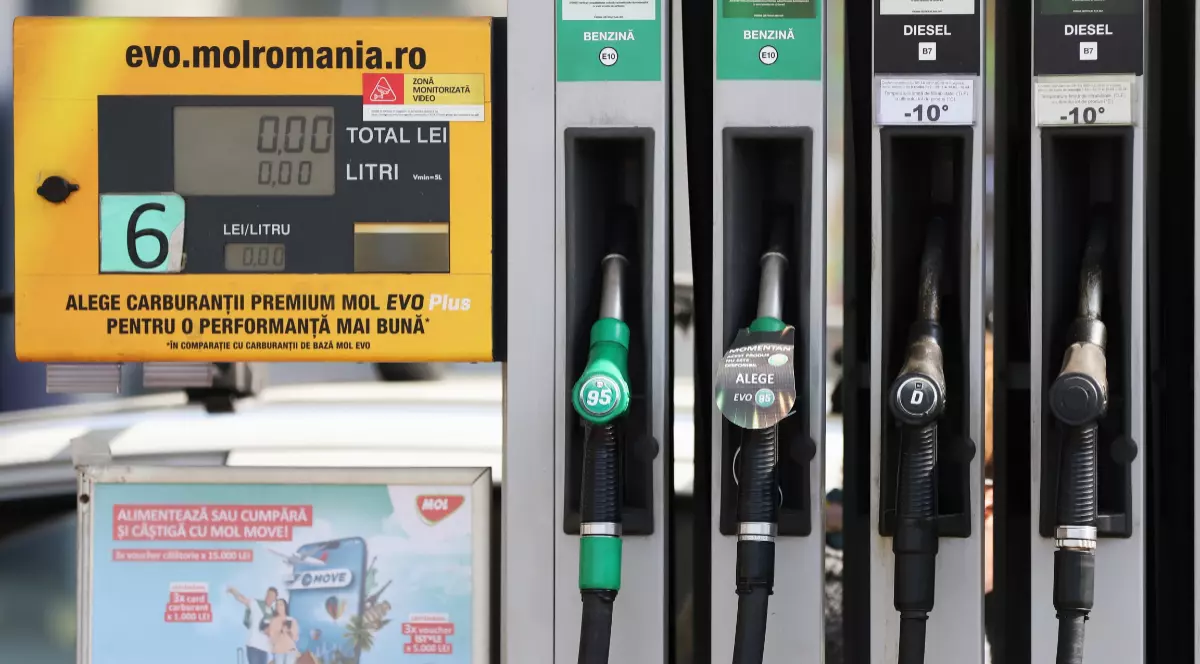 Imaginea prezintă detaliul unei pompe de alimentare dintr-o stație de carburanți, evidențiind pistoalele pentru benzină și motorină alături de ecranul digital de afișare a costului și litrajului.