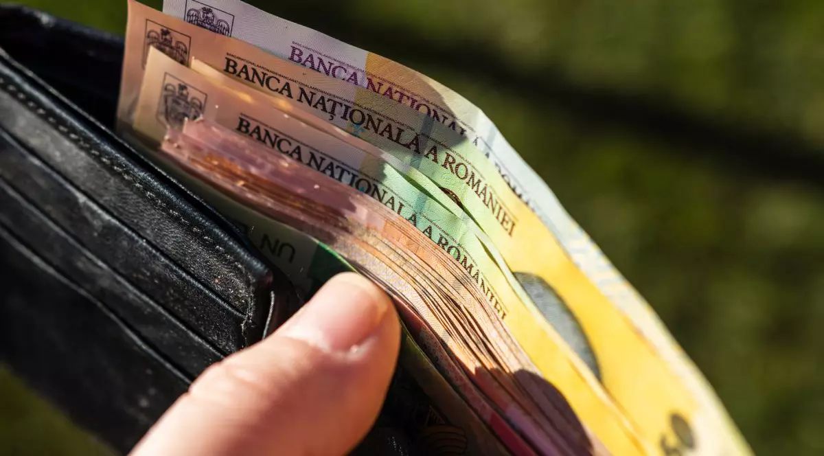 Portofel de culoare neagră ținut în mână, deschis, și în care se află bancnote de 50 și 10 lei