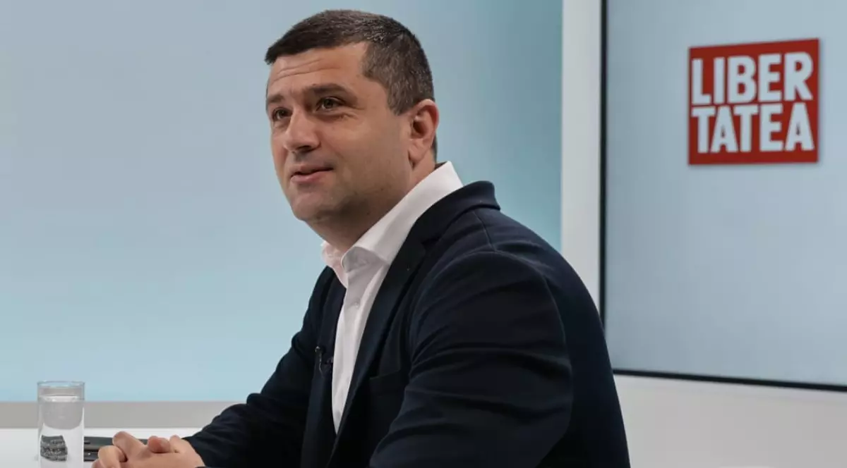 Ministrul Apărării Naționale, Radu Miruță, în platoul Libertatea, în timpul unui interviu. Stă la masă, îmbrăcat în costum și zâmbește